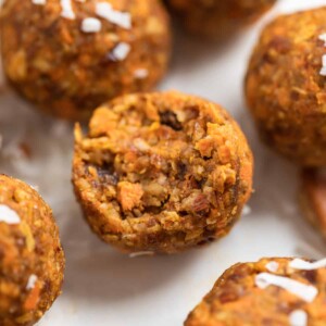 No bake carrot cake bites on counter with shredded coconut.
