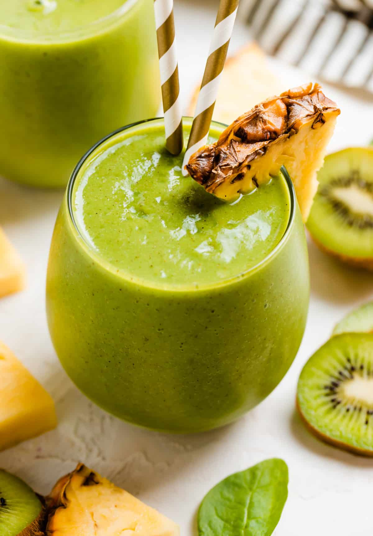 Pineapple kiwi smoothie in glass with pineapple and kiwi slices.
