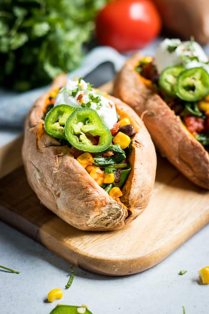 Sweet potatoes stuffed with veggies and spices on wood cutting board.