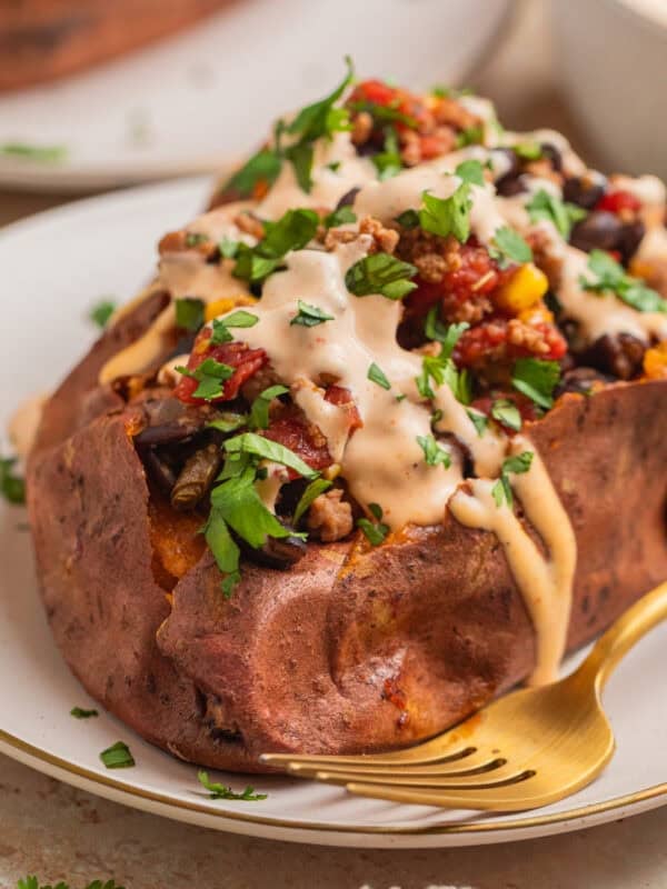 Taco stuffed sweet potato on plate topped with cream sauce.