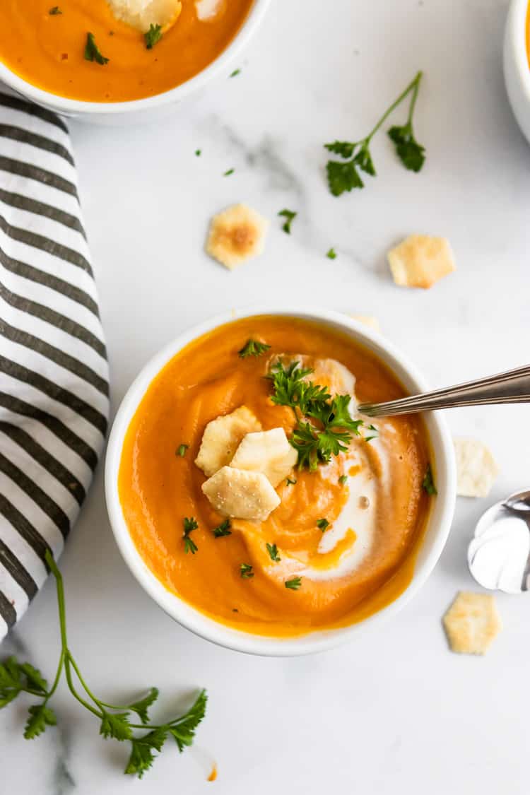 Sweet Potato and carrot soup in white bowl with crackers and spoon.