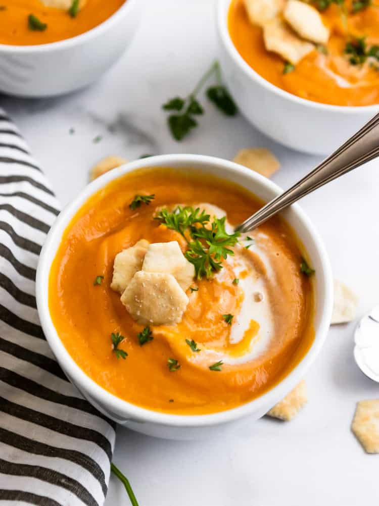 Bowl of soup with spoon and crackers with swirl of cream.