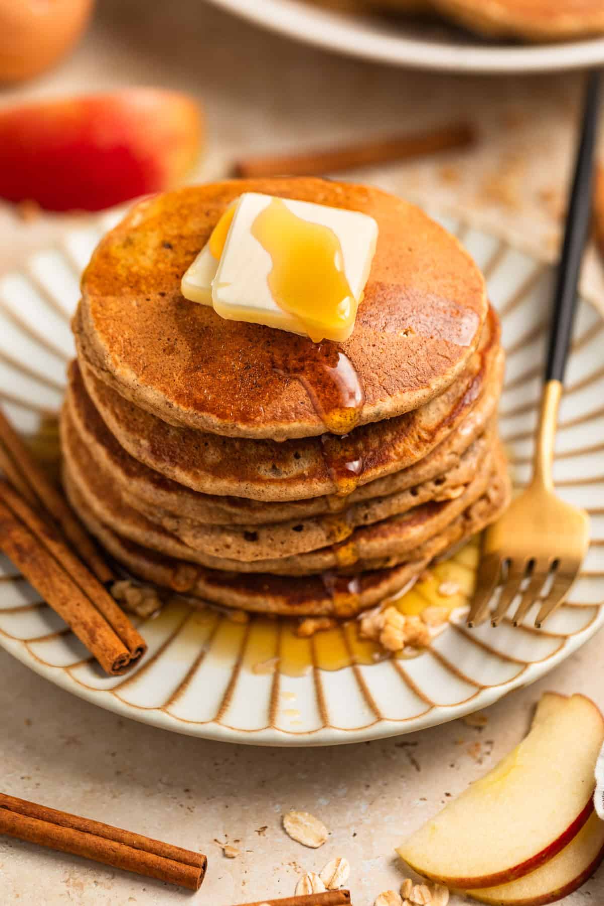 Stack of apple oatmeal pancakes on plate topped with butter and syrup.