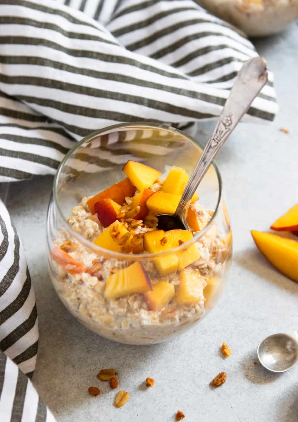Peach Overnight Oats in glass with spoon and fresh peaches.