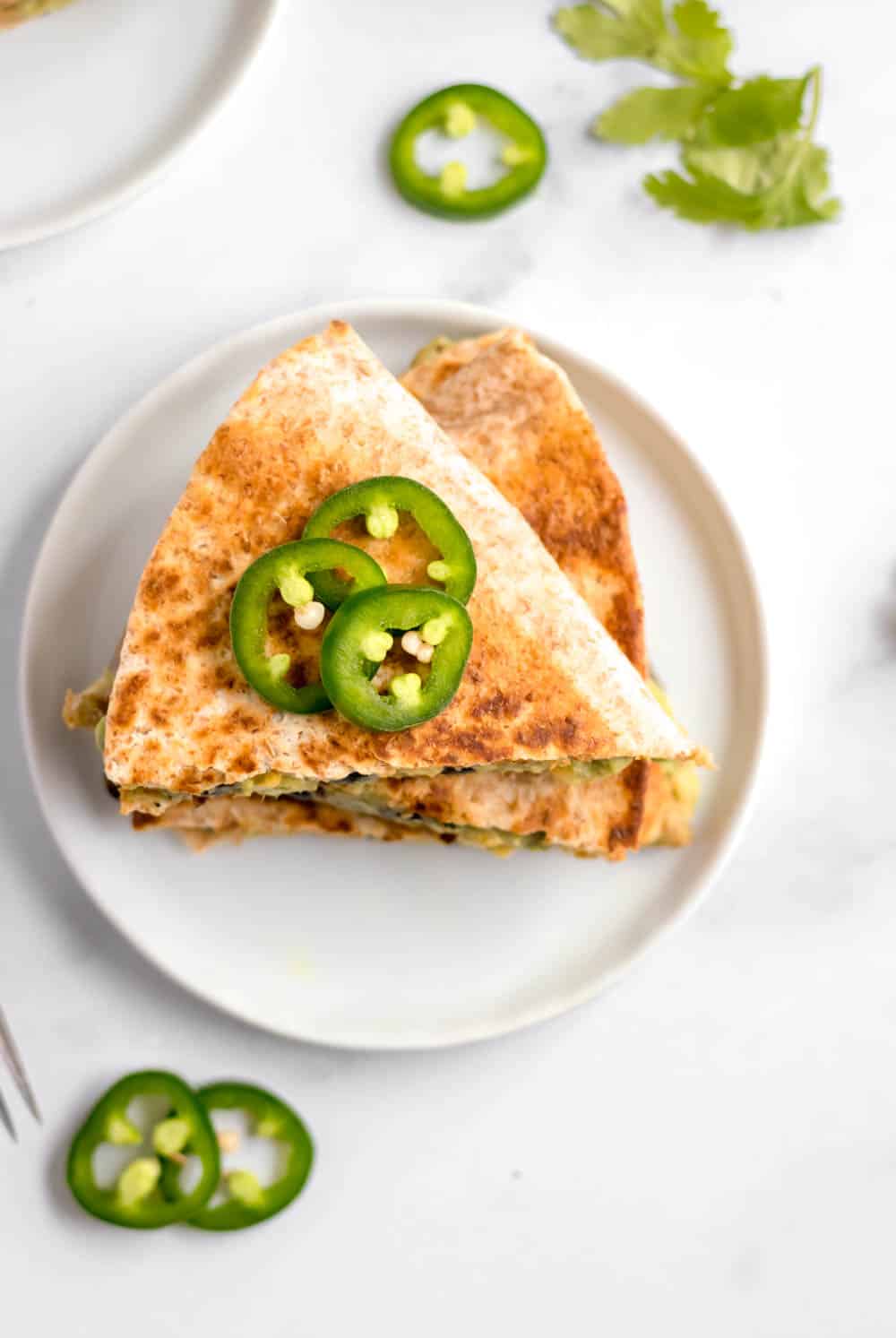 Black bean and avocado quesadilla on white plate with jalapeno.