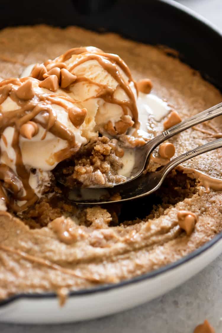 Spoons in skillet cookie with ice cream and peanut butter drizzle.