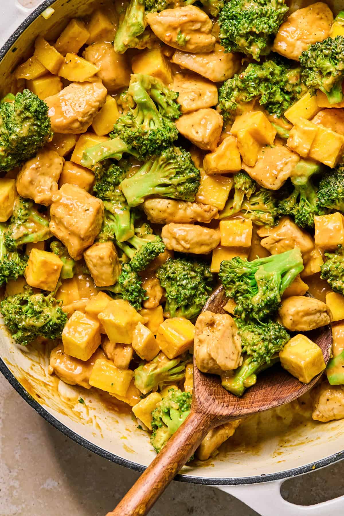 Peanut mango chicken stir fry in skillet with wooden spoon.