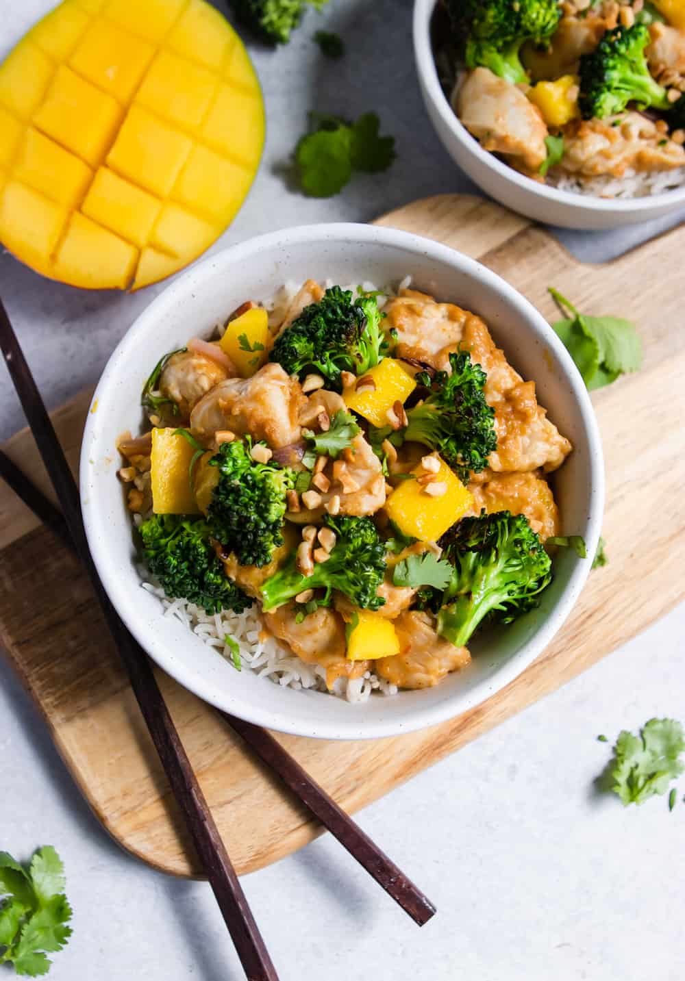 Bowl of chicken stir fry with fresh mango next to it.