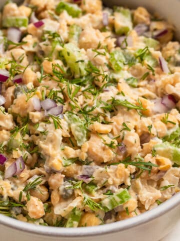Bowl with mashed chickpea mock tuna salad topped with chopped red onion and dill.