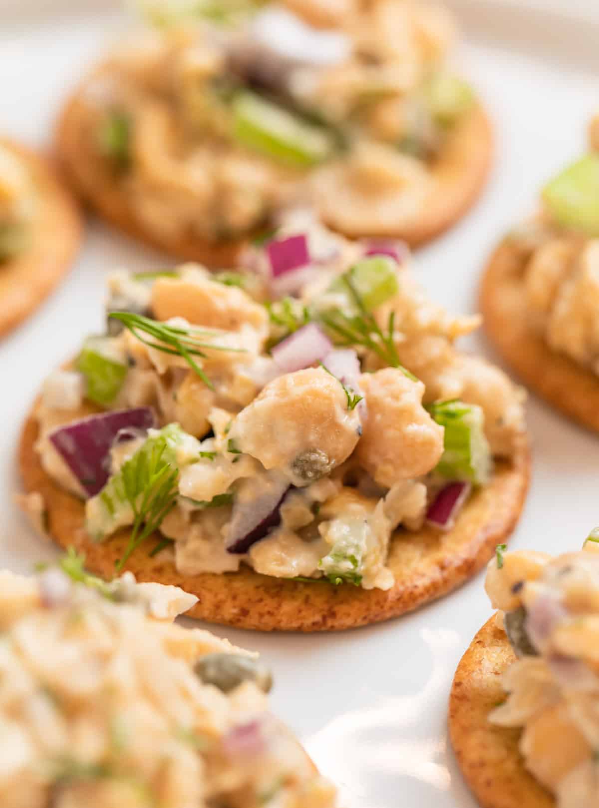 Crackers lined on white plate with vegan tuna on top.