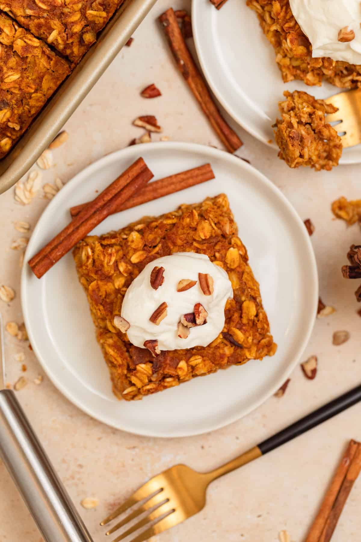 White dish with pumpkin baked oats with cinnamon sticks propped beside it.