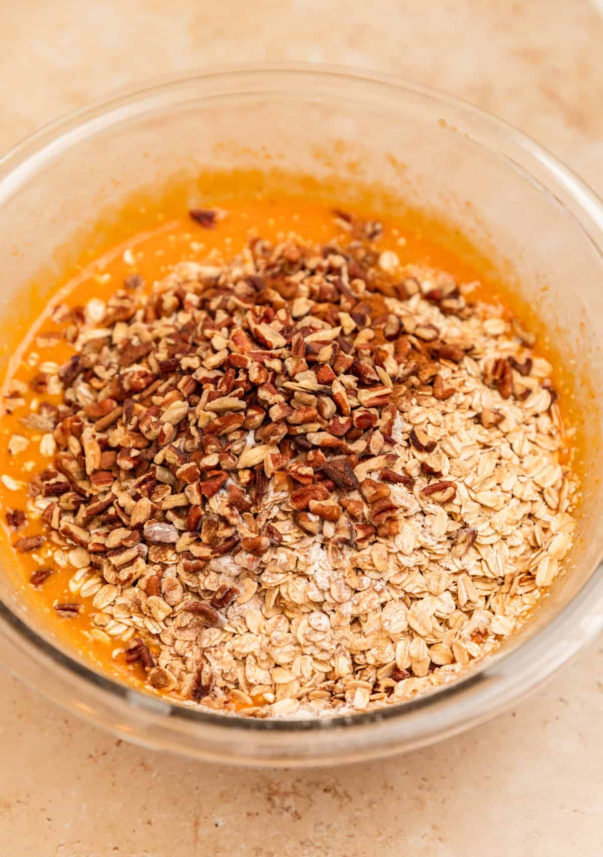 Rolled oats and pecans added to wet ingredients in bowl.