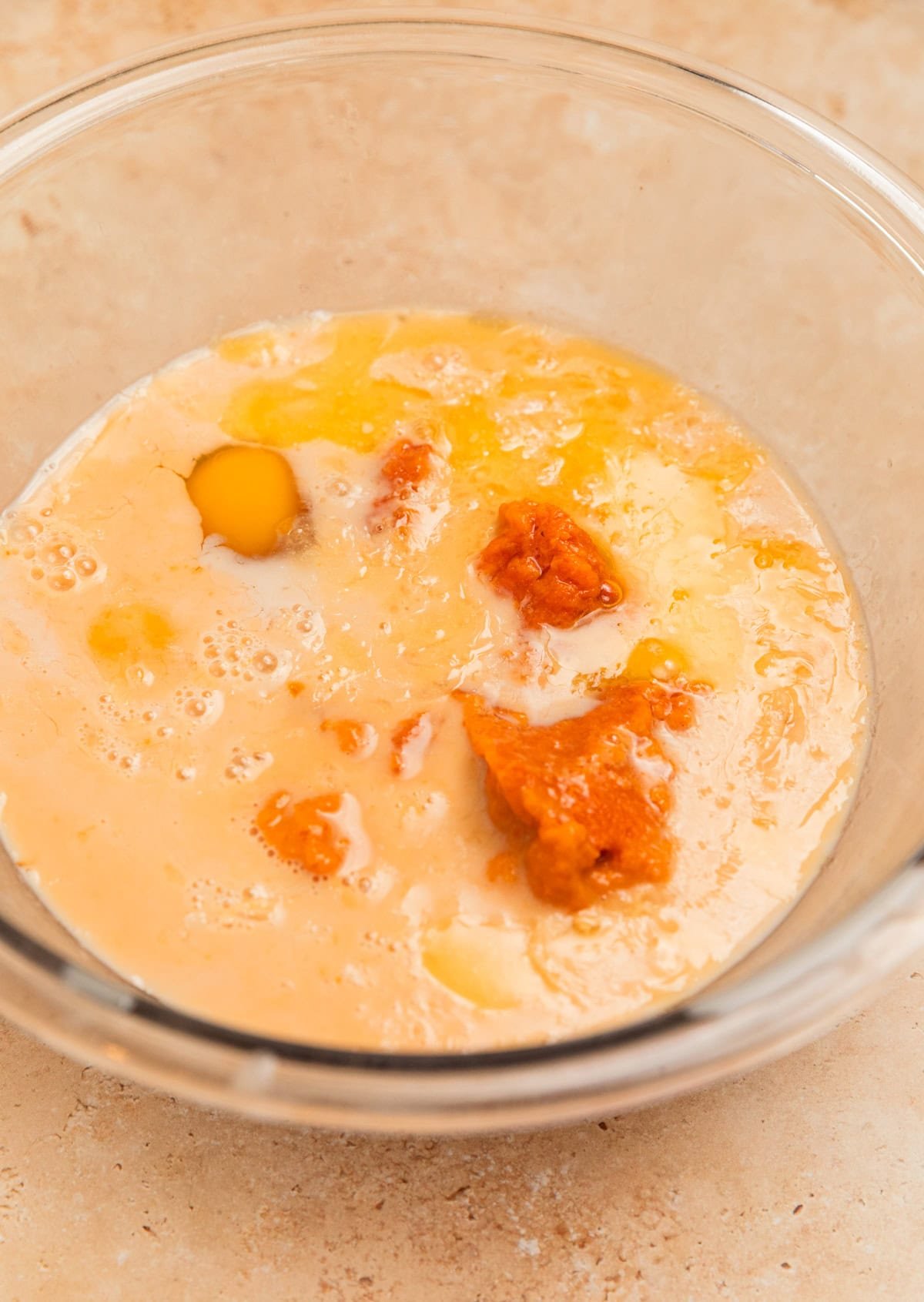 Milk, pumpkin, eggs and maple syrup in glass mixing bowl.