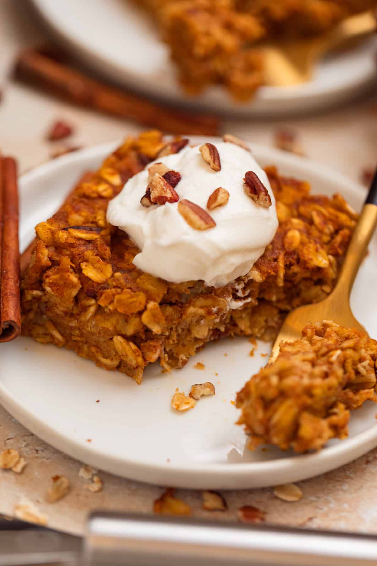 Baked pumpkin oat meal on white plate with greek yogurt and pecans on top.