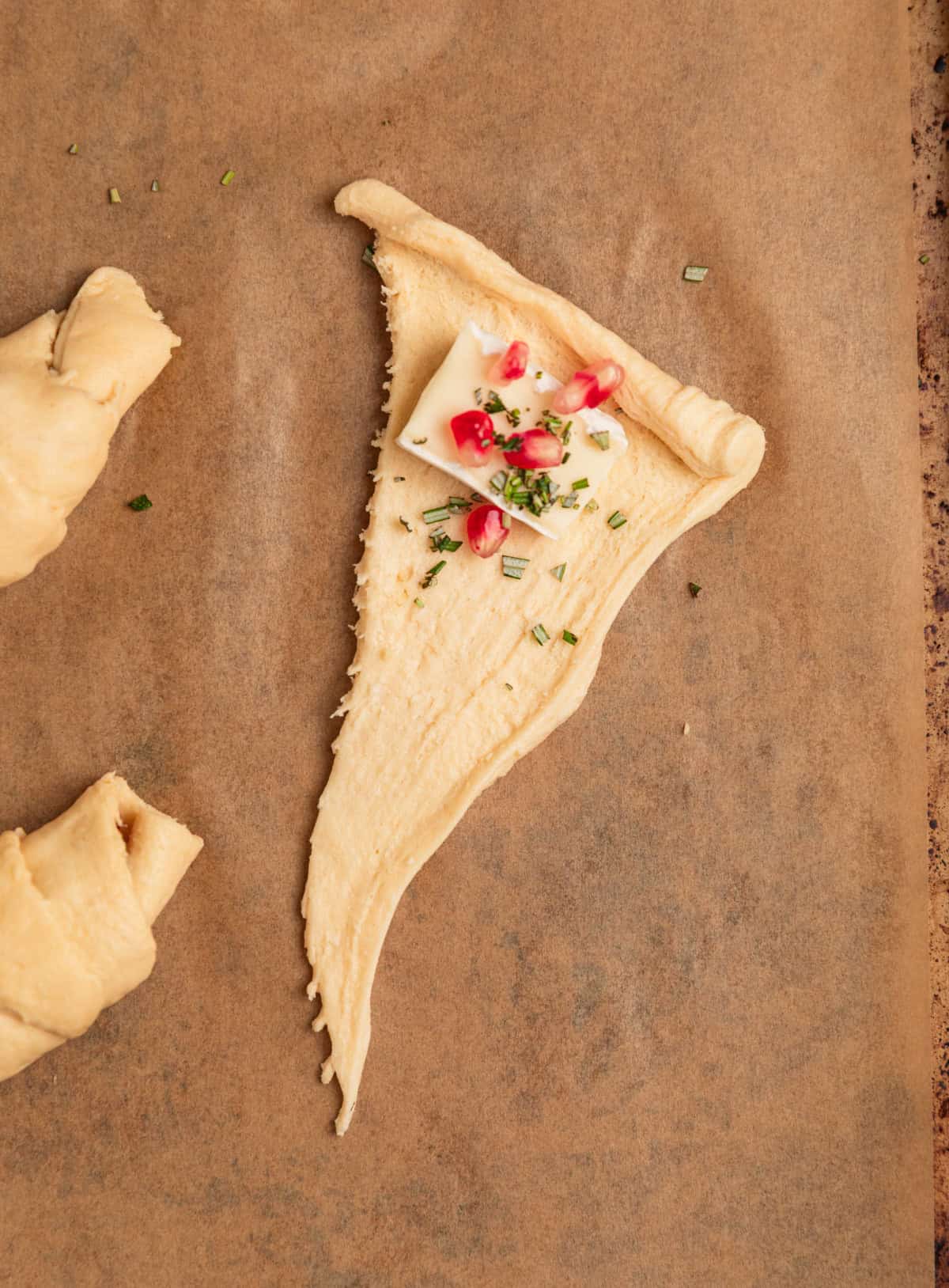 Crescent roll dough on parchment with brie, rosemary and pomegranate. 