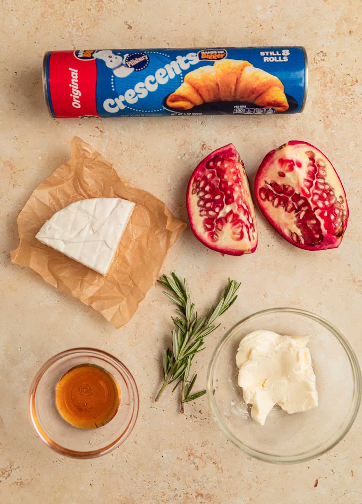 Crescent roll package, wedge of brie, rosemary sprigs and other ingredients on surface.