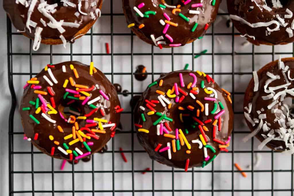 Chocolate glazed whole wheat donuts with sprinkles on cooling rack.