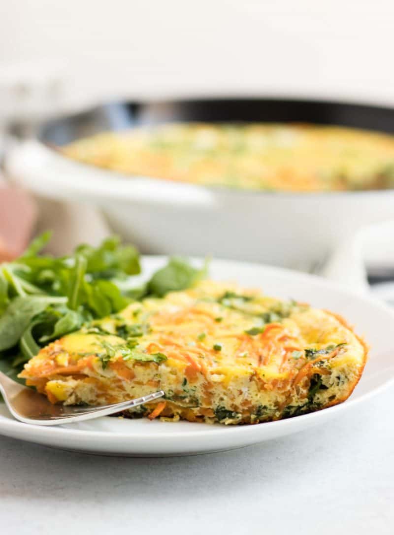 Slice of sweet potato frittata with baby arugula on plate with fork.