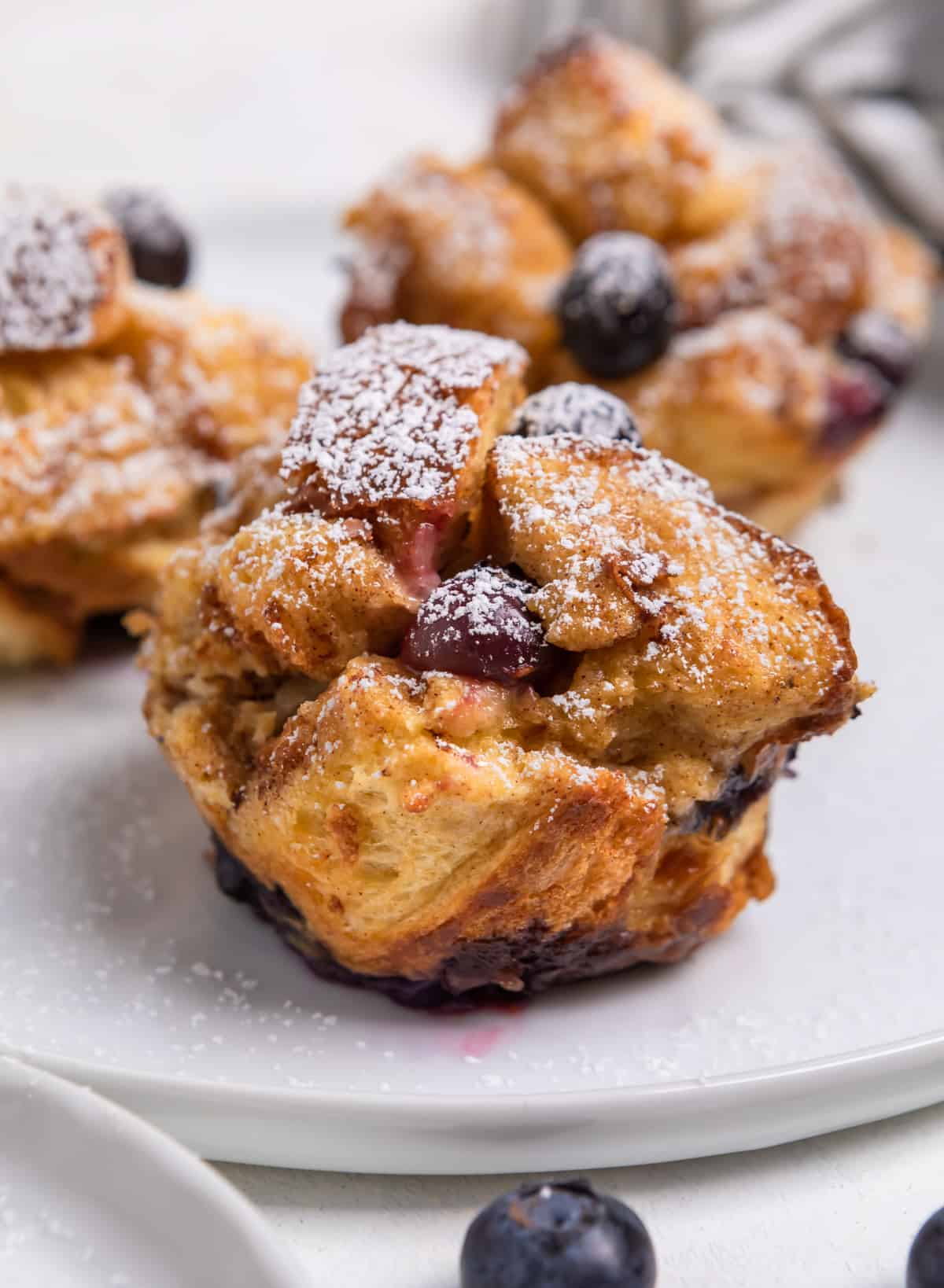 Blueberry French Toast cups on white plate with powdered sugar dusted over top.