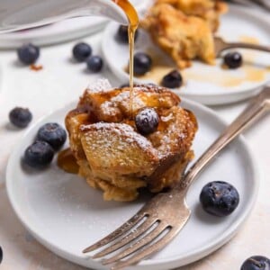 Maple poured over blueberry French toast muffin on white dish with fork.