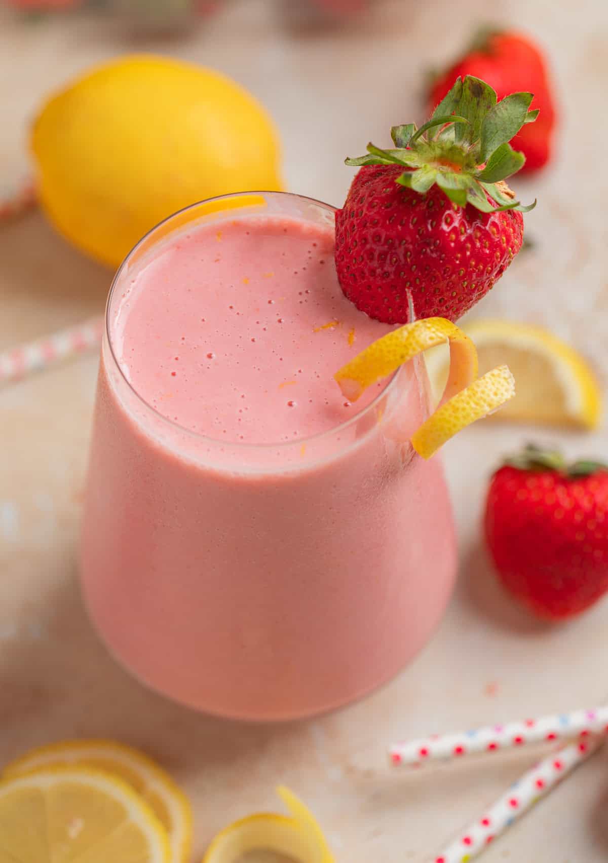 Smoothie in glass with lemon and strawberries and straws surrounding.