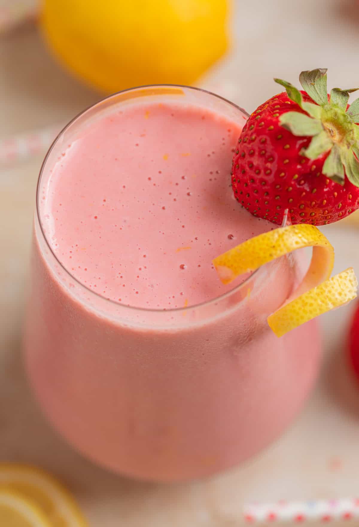 Strawberry lemonade smoothie in glass with lemon zest and strawberry garnish.