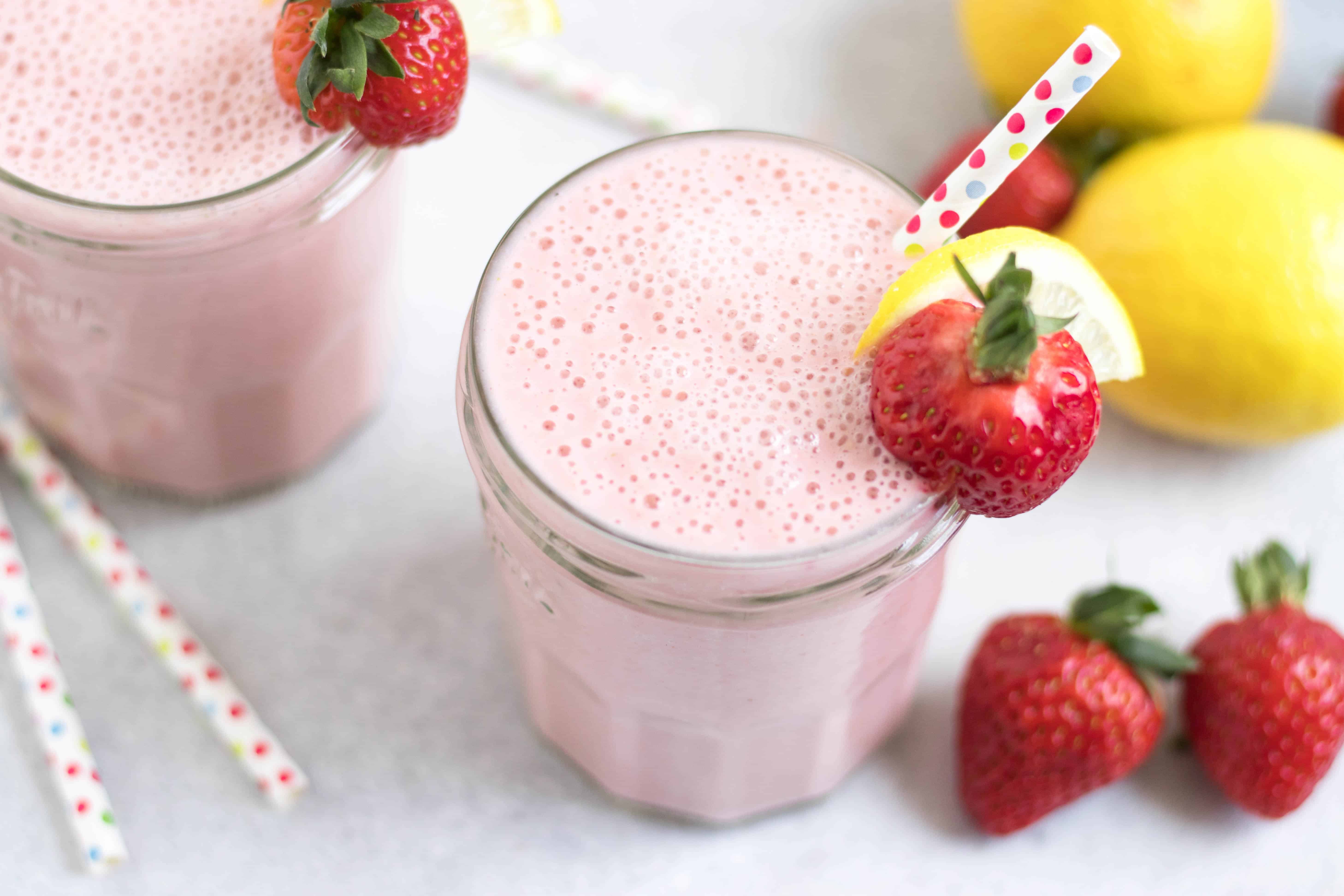 Strawberry lemonade smoothie with straw and fruit garnish.