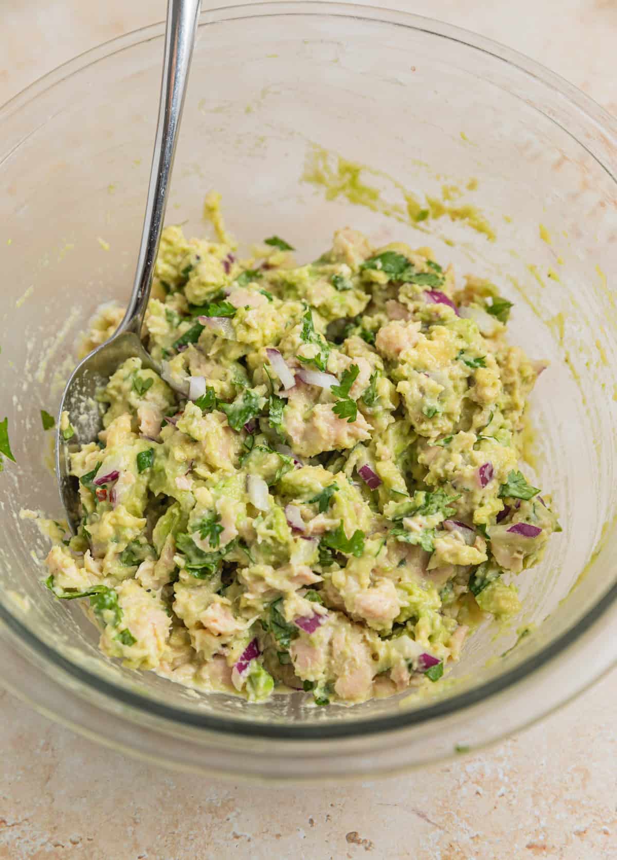 Avocado tuna salad mixed in bowl with spoon.