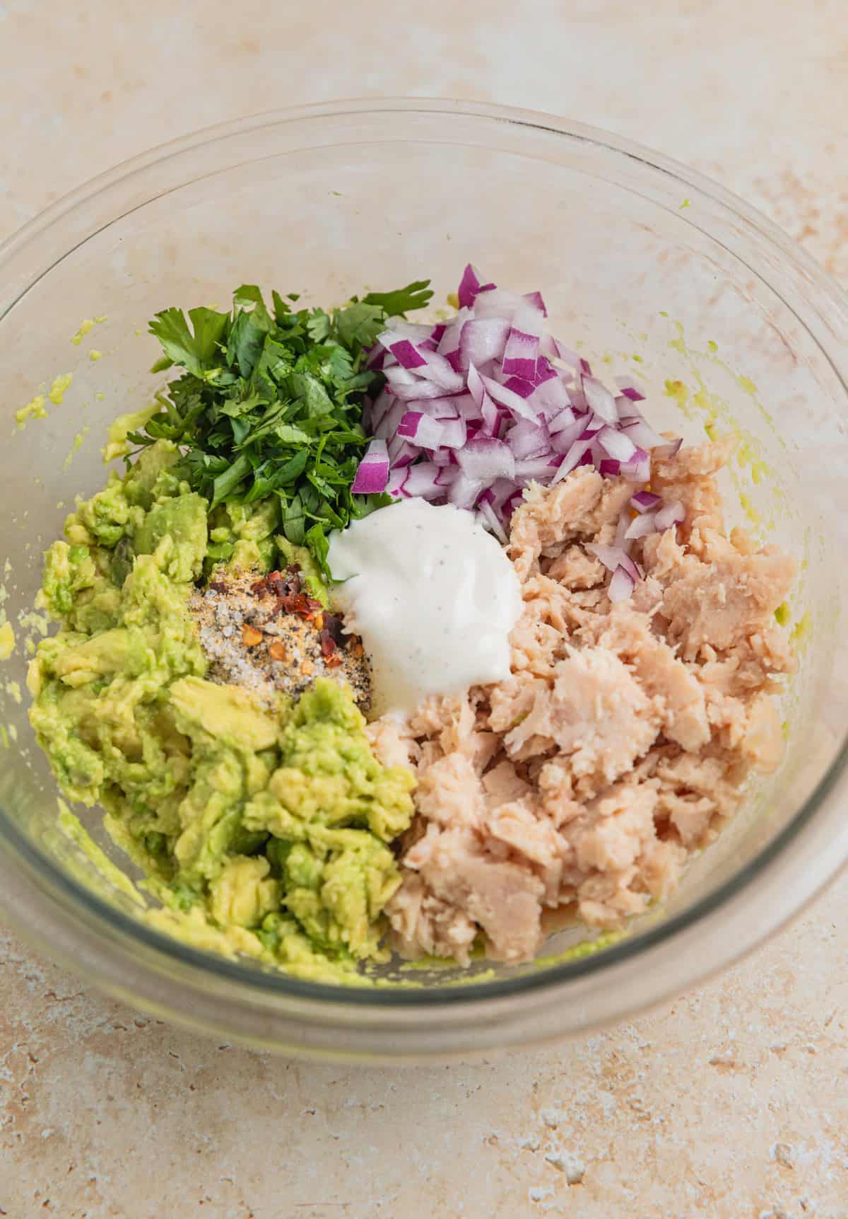 Flaked tuna, red onion, cilantro, avocado and Ranch dressing in mixing bowl before being stirred.