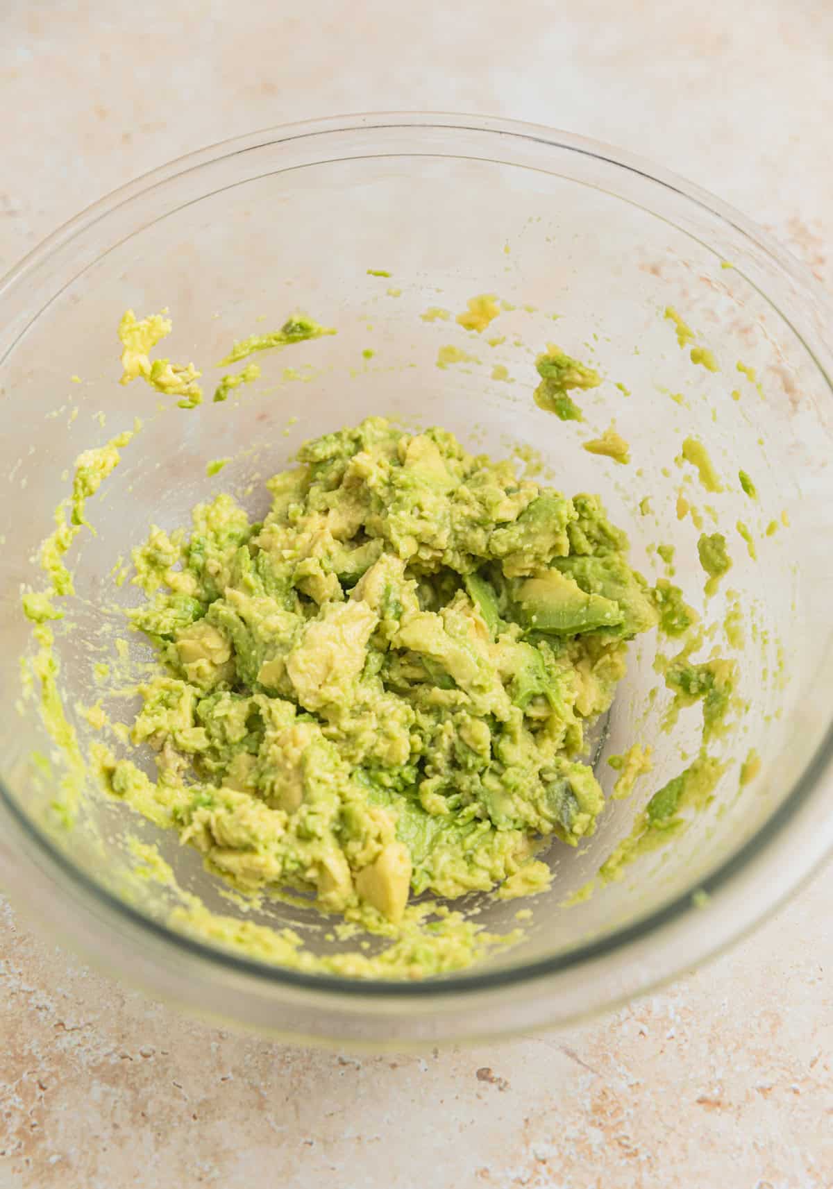 Glass mixing bowl with mashed avocado.