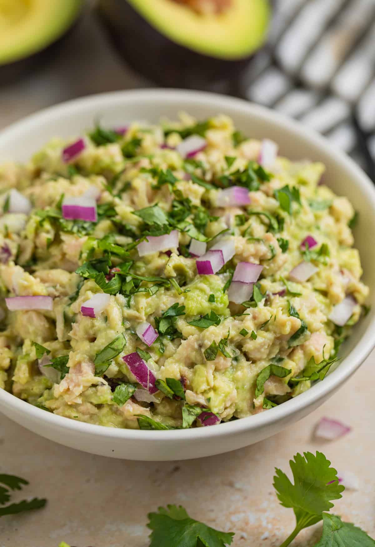Avocado tuna salad in bowl topped with chopped cilantro and diced red onion.