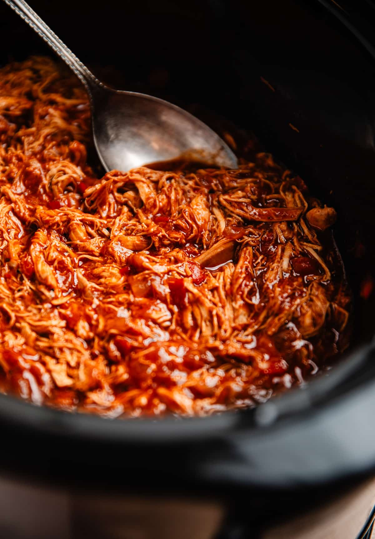 Crock pot with shredded BBQ chicken prepared and serving spoon scooping into it.