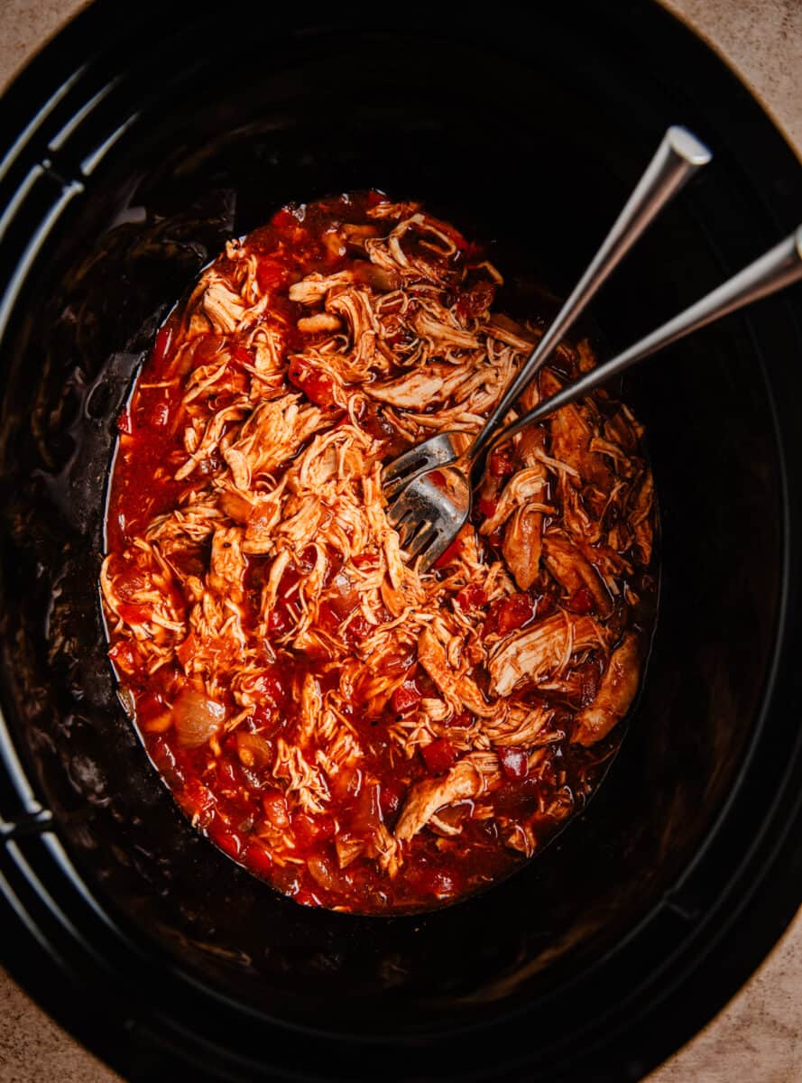 Shredded BBQ chicken with forks in slow cooker pot.