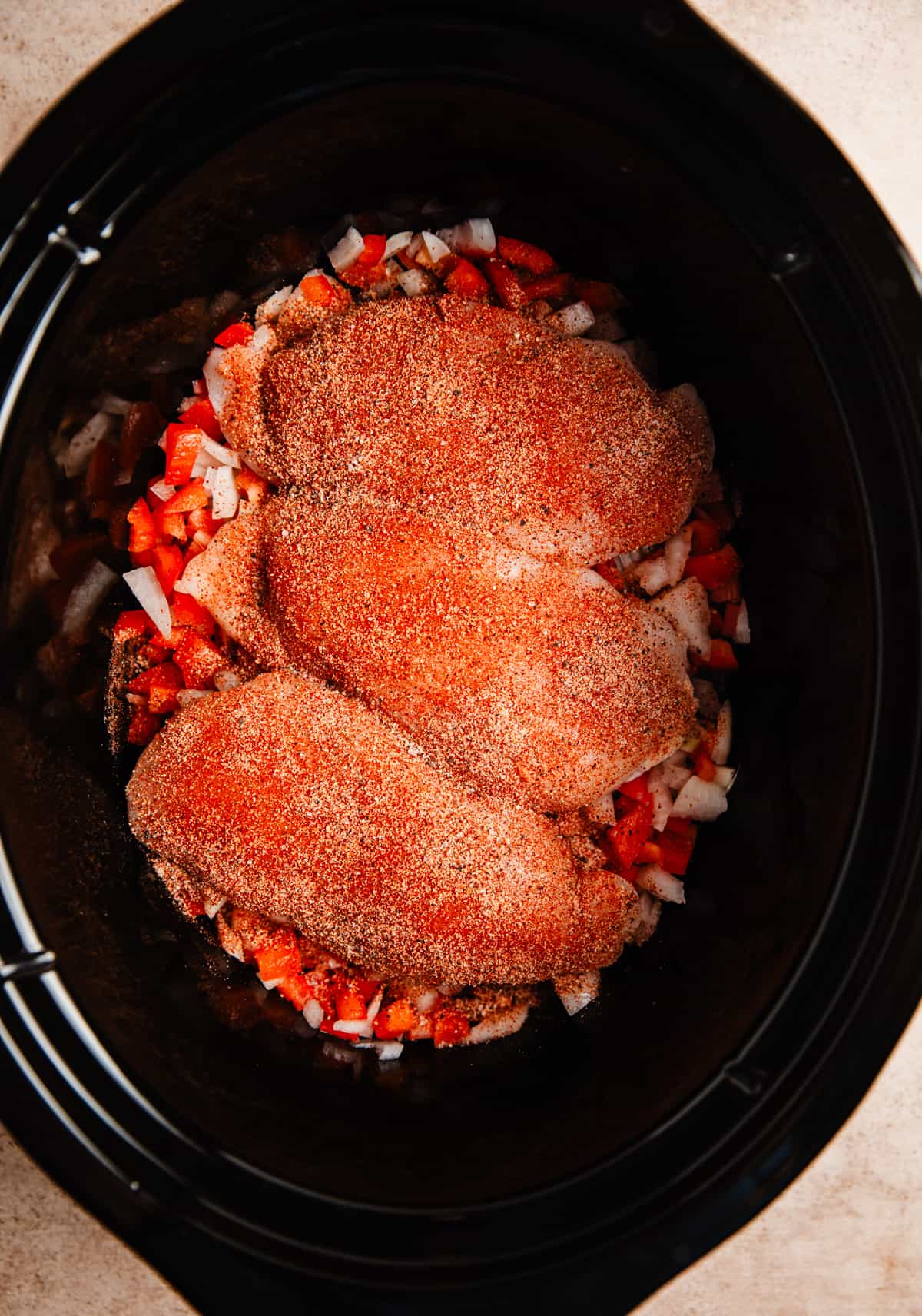 Chicken breasts with spice rub on onions and peppers in crockpot.