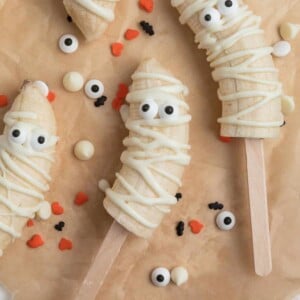 Mummy banana pops with candy eyeballs on parchment.