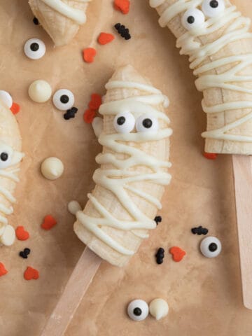 Mummy banana pops with candy eyeballs on parchment.