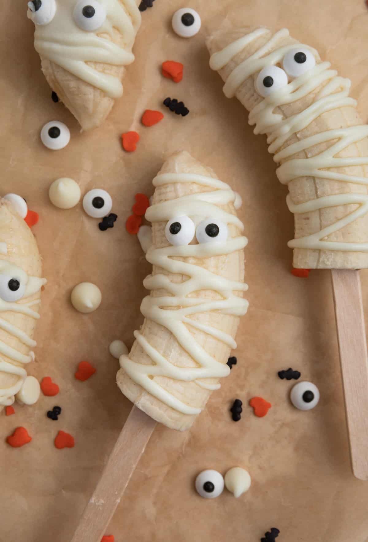 Banana mummy pops with candy eye balls on parchment.
