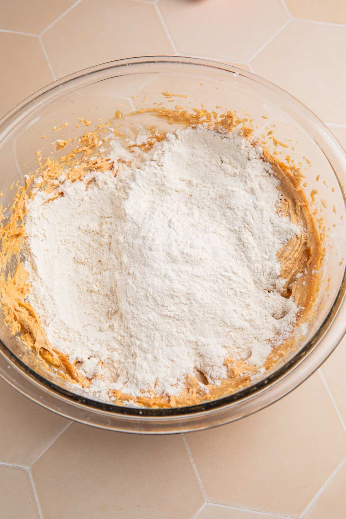 Flour added to peanut butter cookie dough mixture in bowl.