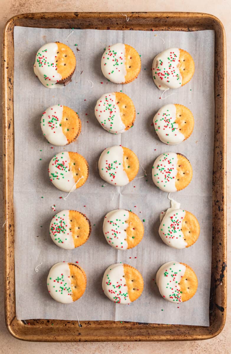 White chocolate dipped cracker sandwich cookies with red and green sprinkles on top.