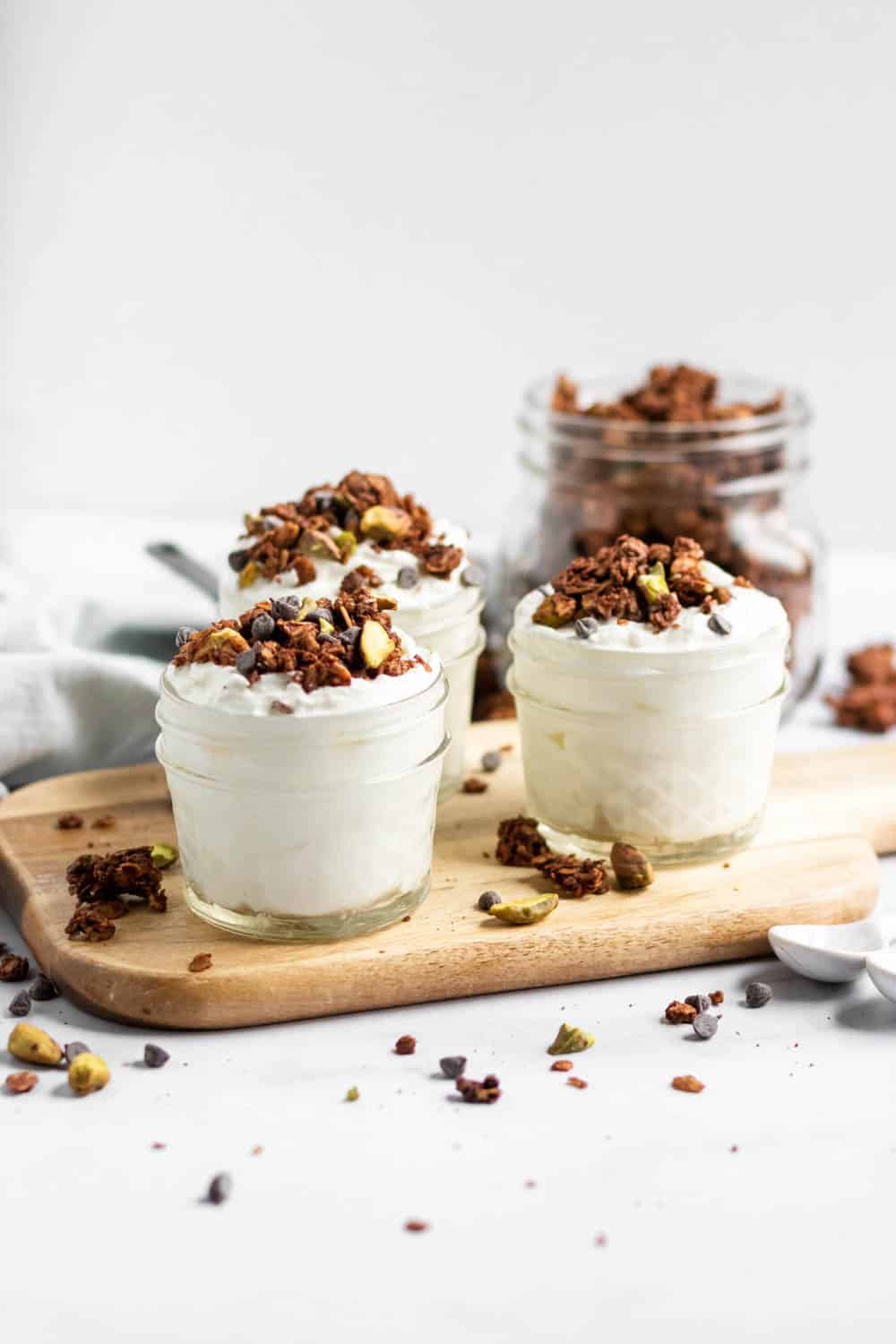 Chocolate granola with chocolate chips and pistachios on yogurt in jars.