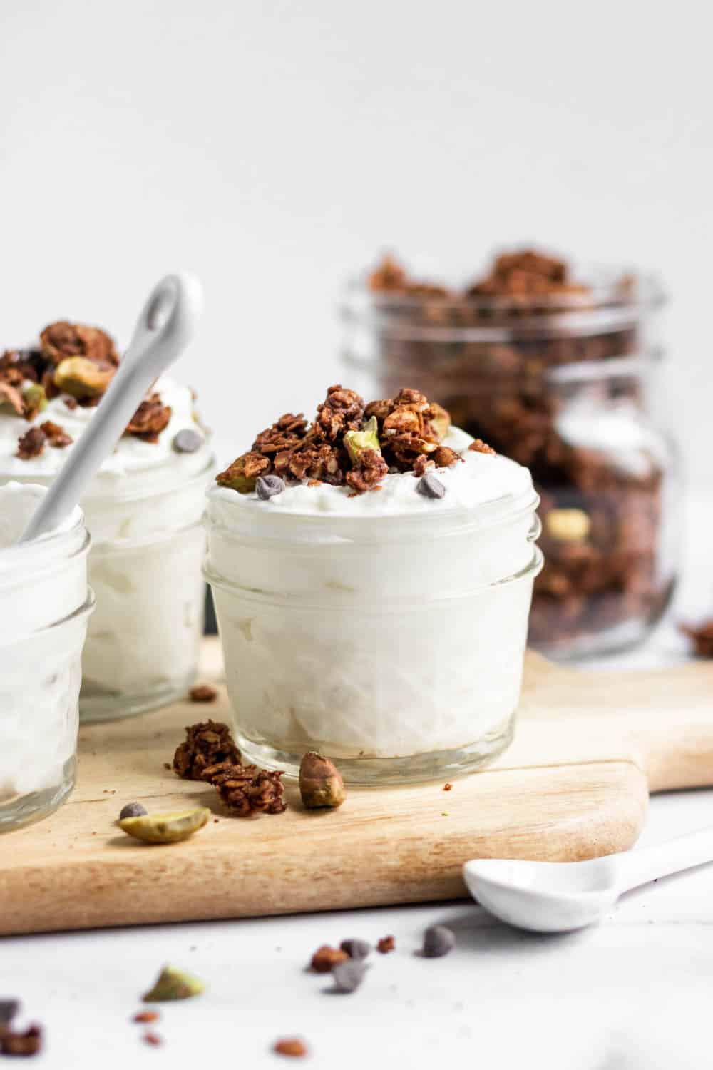 Chocolate Granola in jars over yogurt with pistachios.