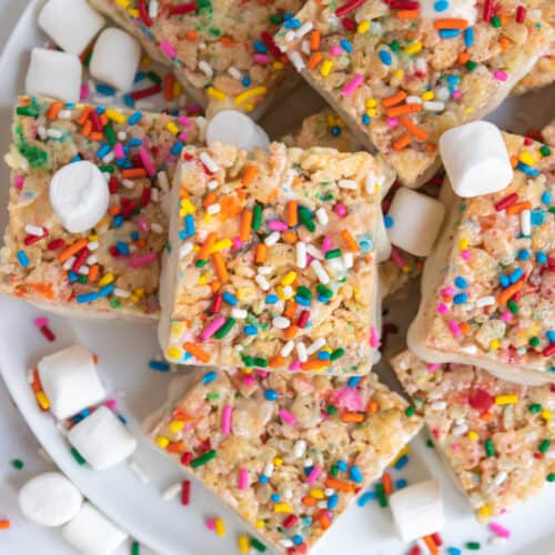 Overhead view of birthday cake rice krispie treats on white plate with sprinkles and marshmallows.