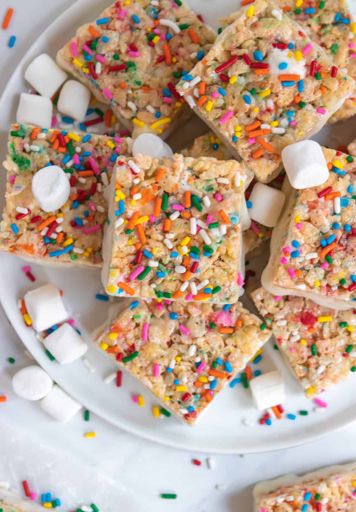 Overhead view of funfetti rice krispie treats on plate with sprinkles and extra marshmallows.