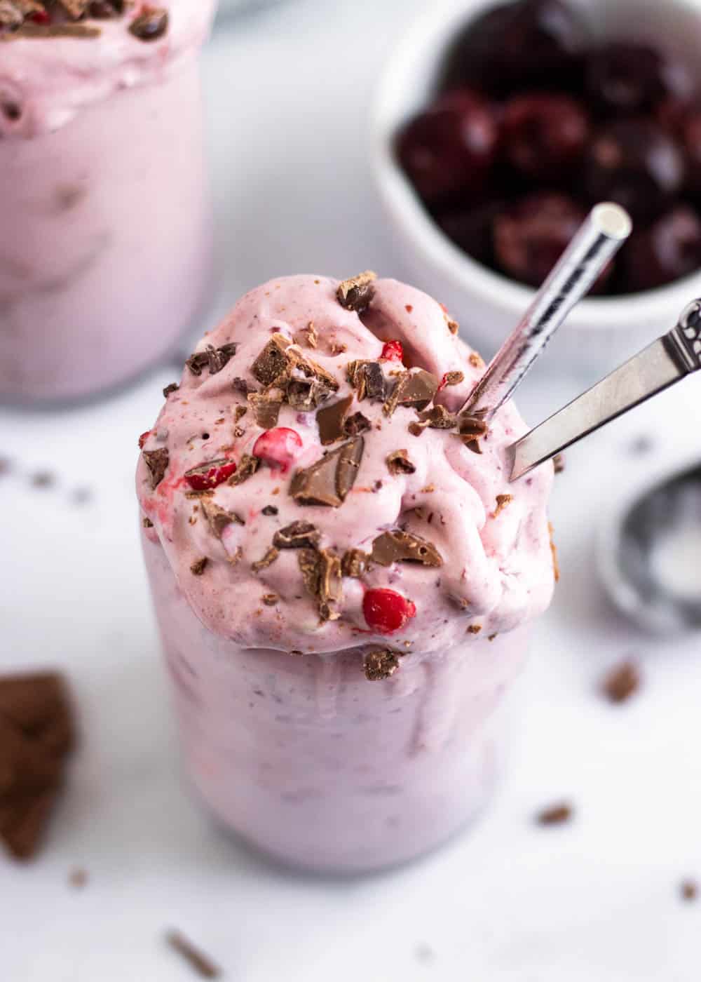 Cherry milkshake with chocolate in and straw and spoon.