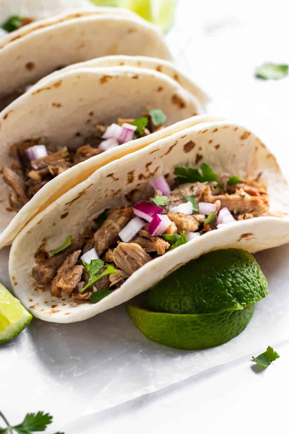 Carnitas tacos topped with red onion and cilantro.