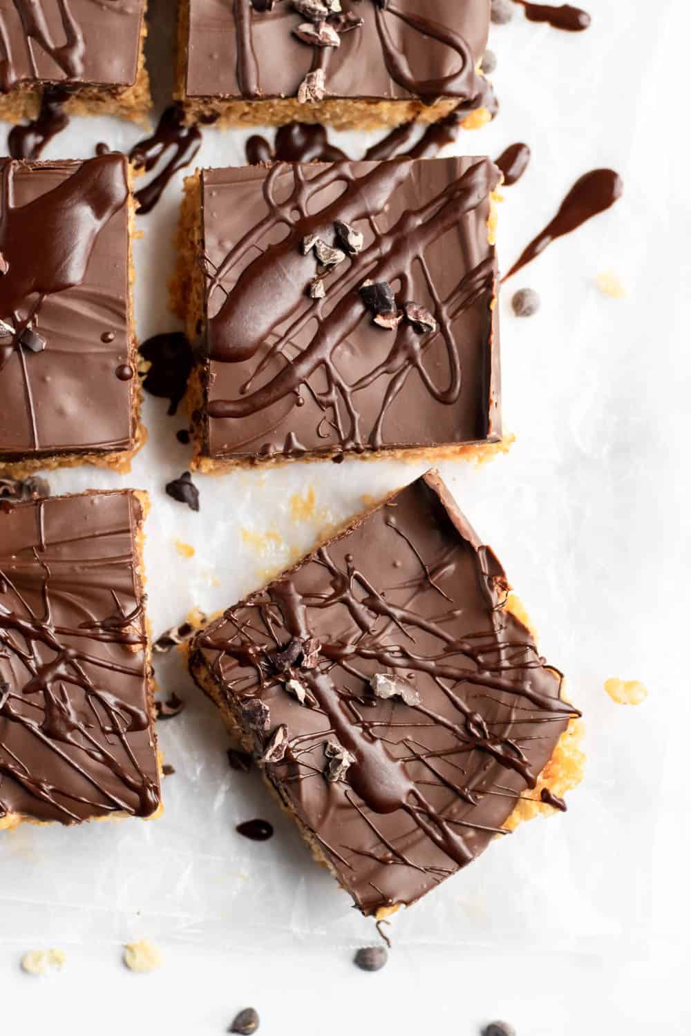 Chocolate peanut butter rice krispie treats with chocolate drizzle and chocolate chips on parchment.