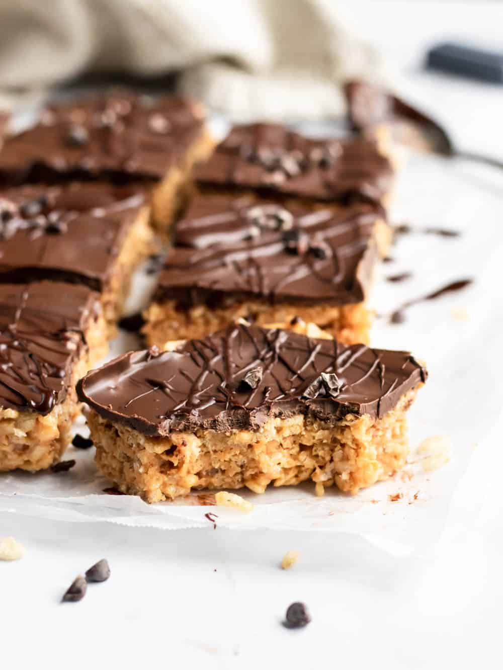 Sliced rice crispy treats with peanut butter and chocolate layer with bite taken out of front piece.