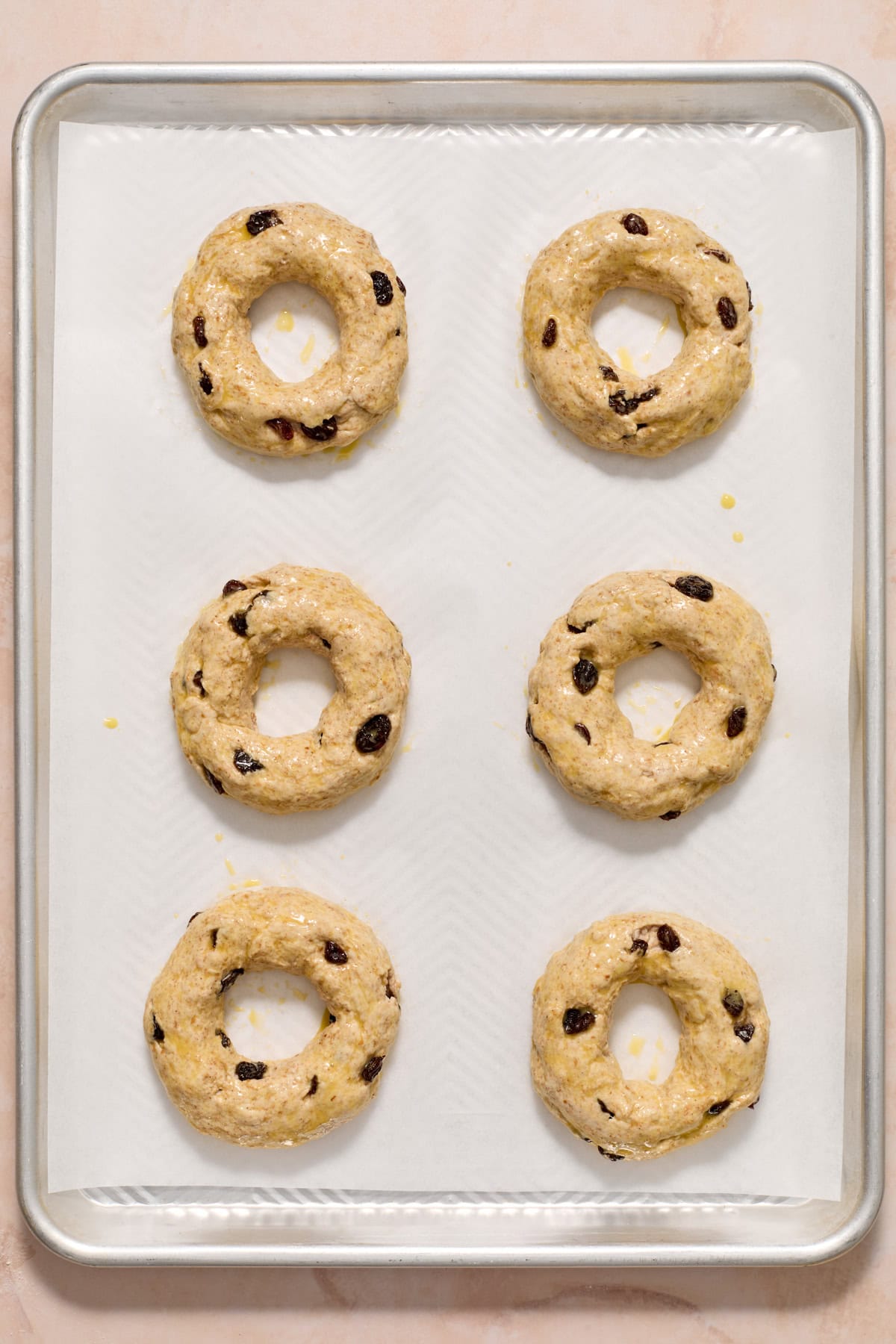 Egg washed cinnamon raisin bagels on cookie sheet before baking.