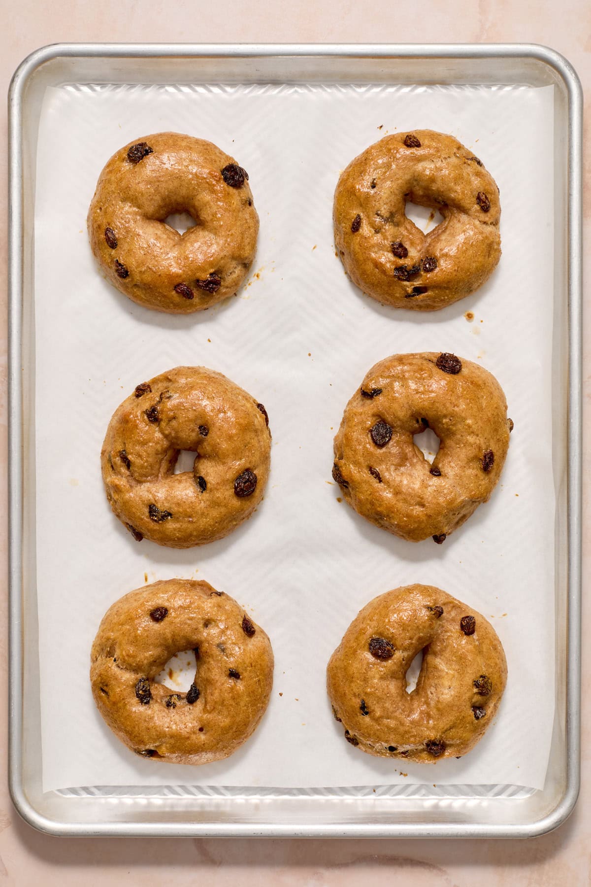 Baked cinnamon raisin bagels on parchment lined pan.