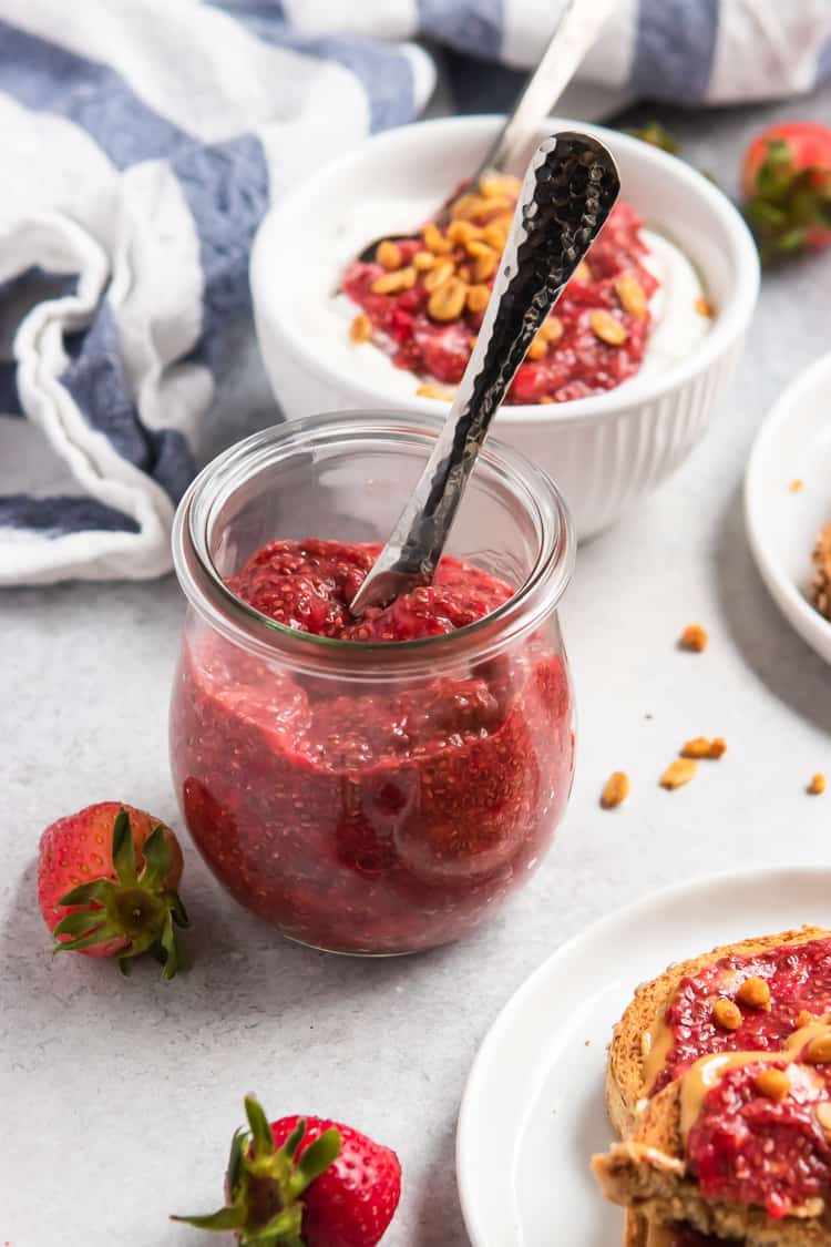 Jar of vegan chia seed jam with knife and berries beside it.